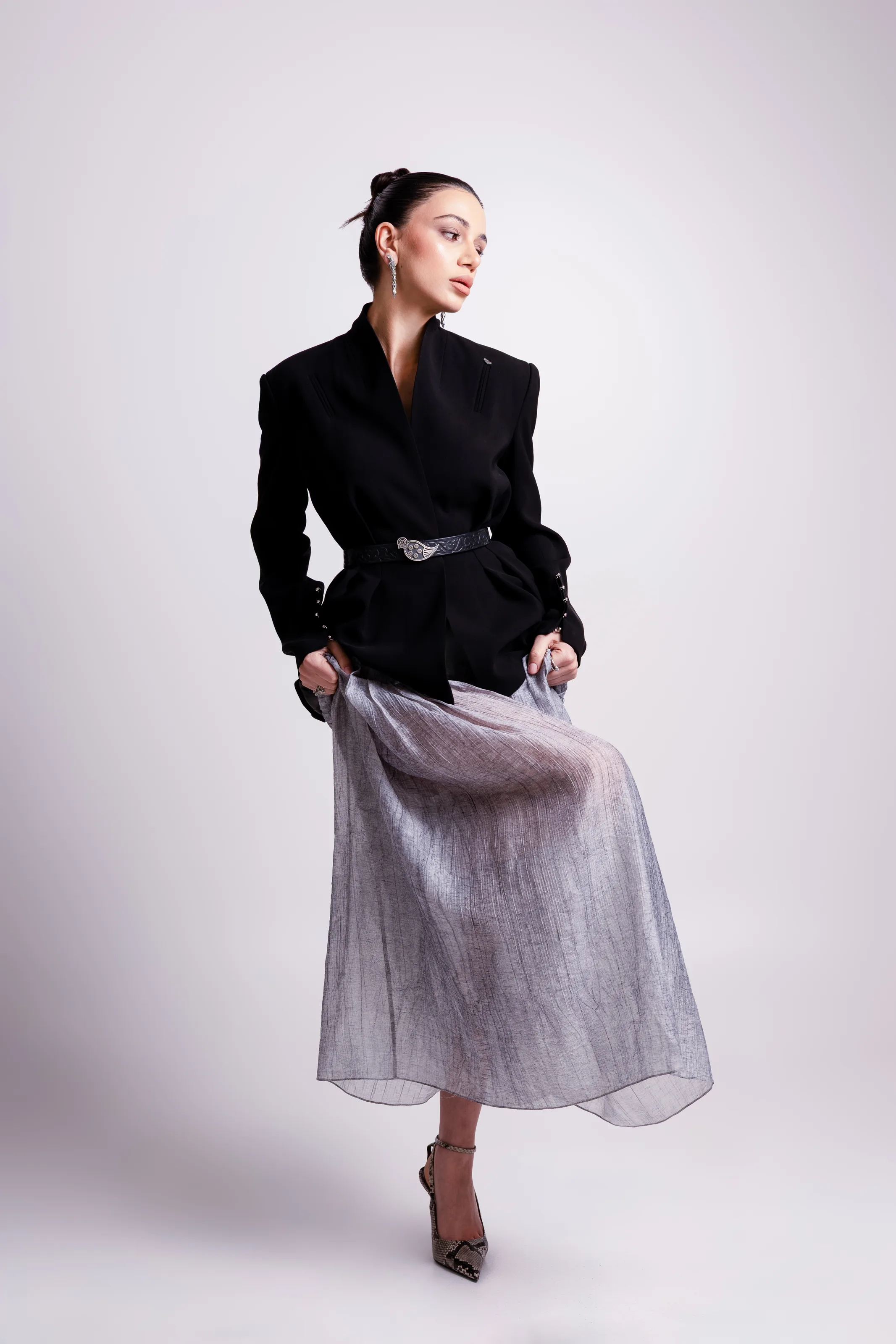 The belted black jacket worn over a sheer grey skirt, the skirt held out to one side
