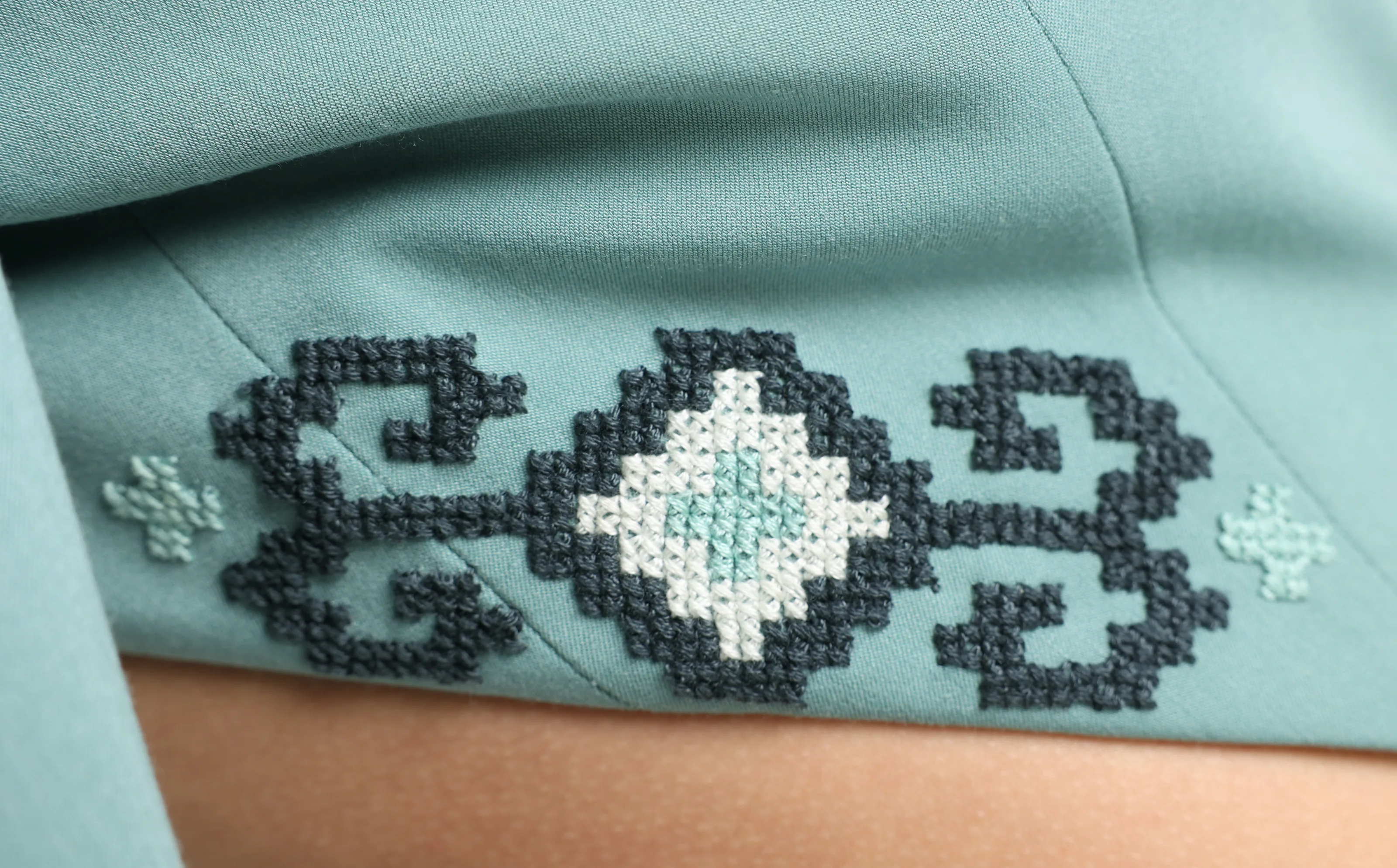 Detail of hand cross-stitch on sage cloth: a charcoal medallion with a cream and mint centre