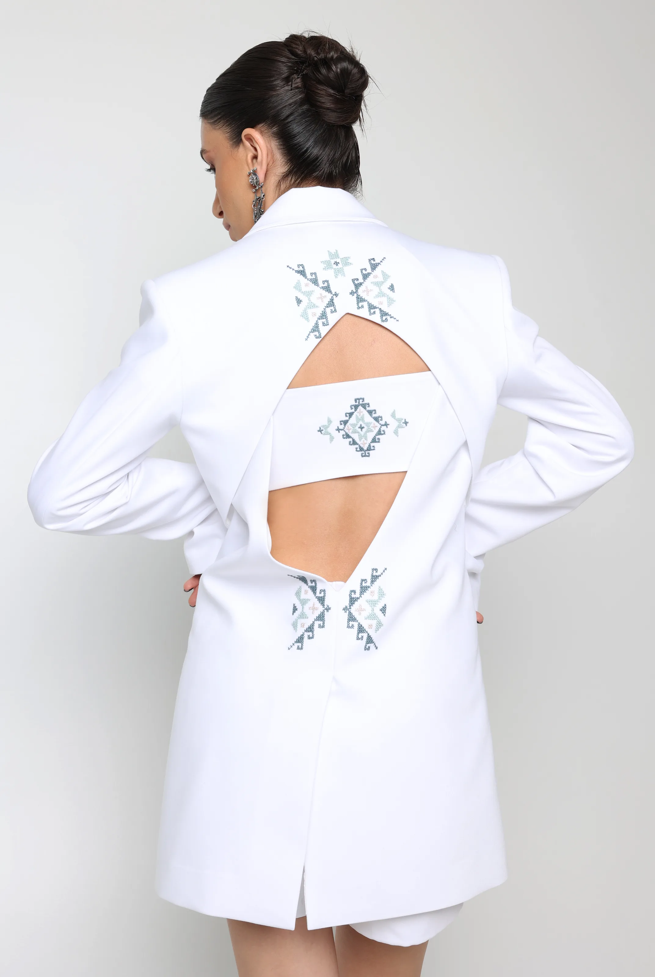 White tailored jacket from behind with two cut-outs divided by a band, embroidered in soft blue, green and pink